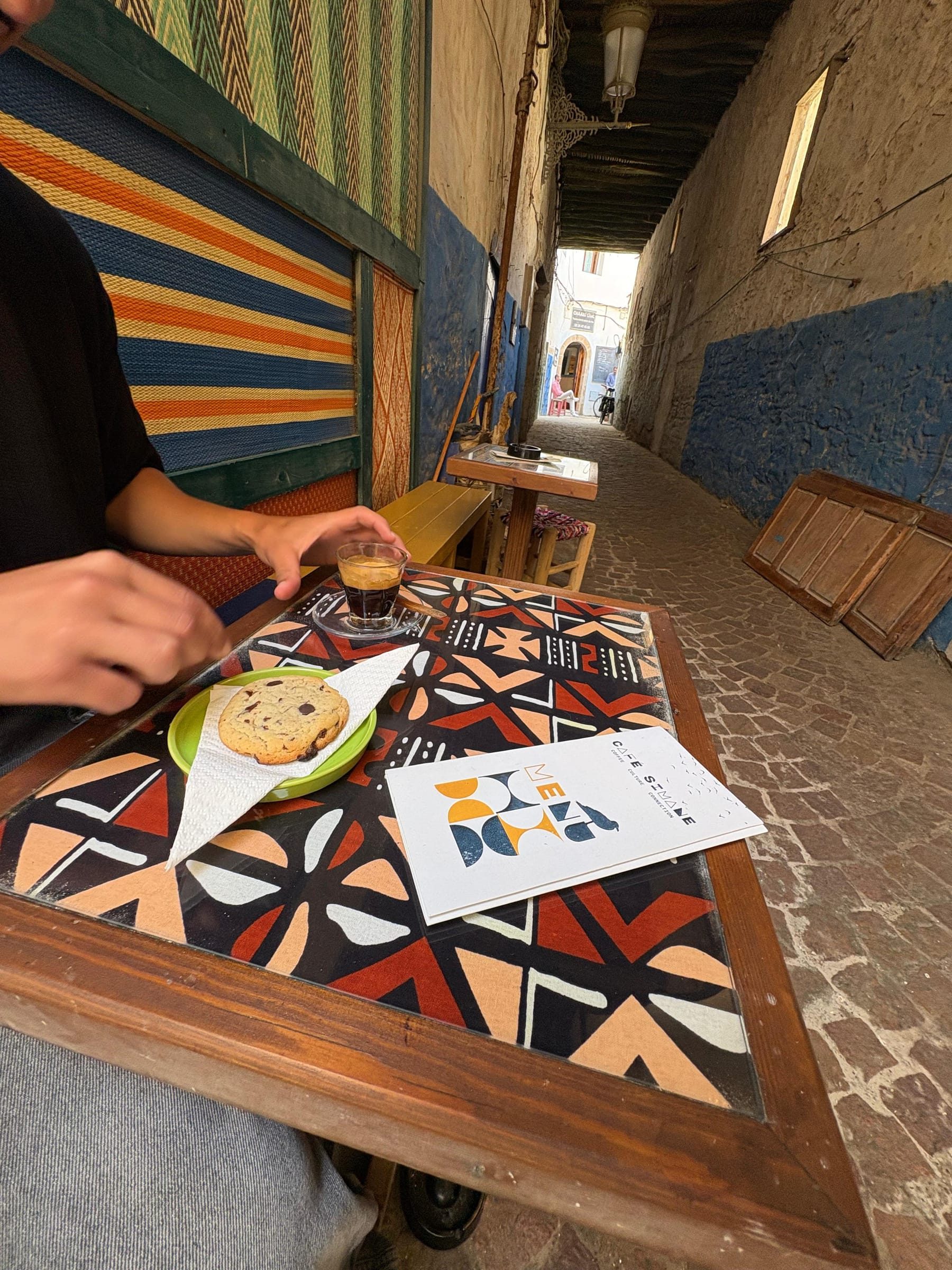 Espresso and a cookie on the table, the Simane Café sign visible down the alley