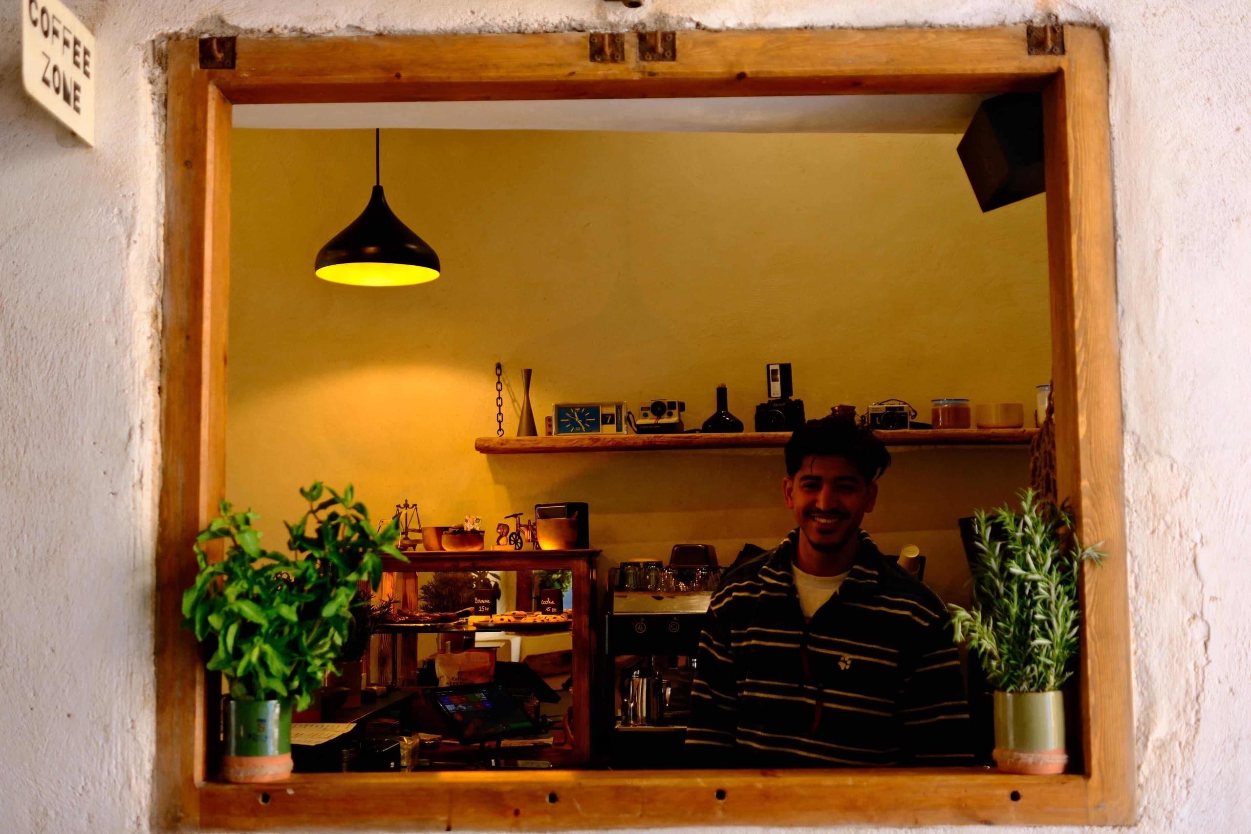 A barista smiling behind the espresso machine at Simane's counter window, in Essaouira's medina