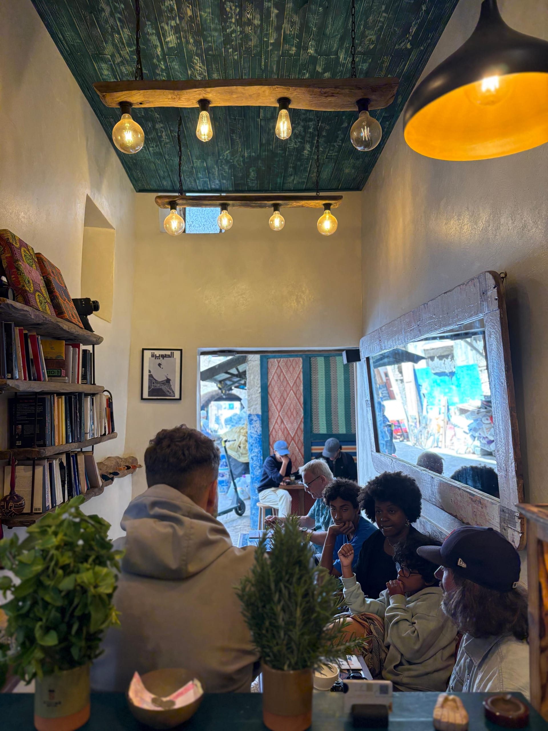 The Simane room from above, warm bulbs over the bookshelves and tables, a mirror reflecting the blue medina street
